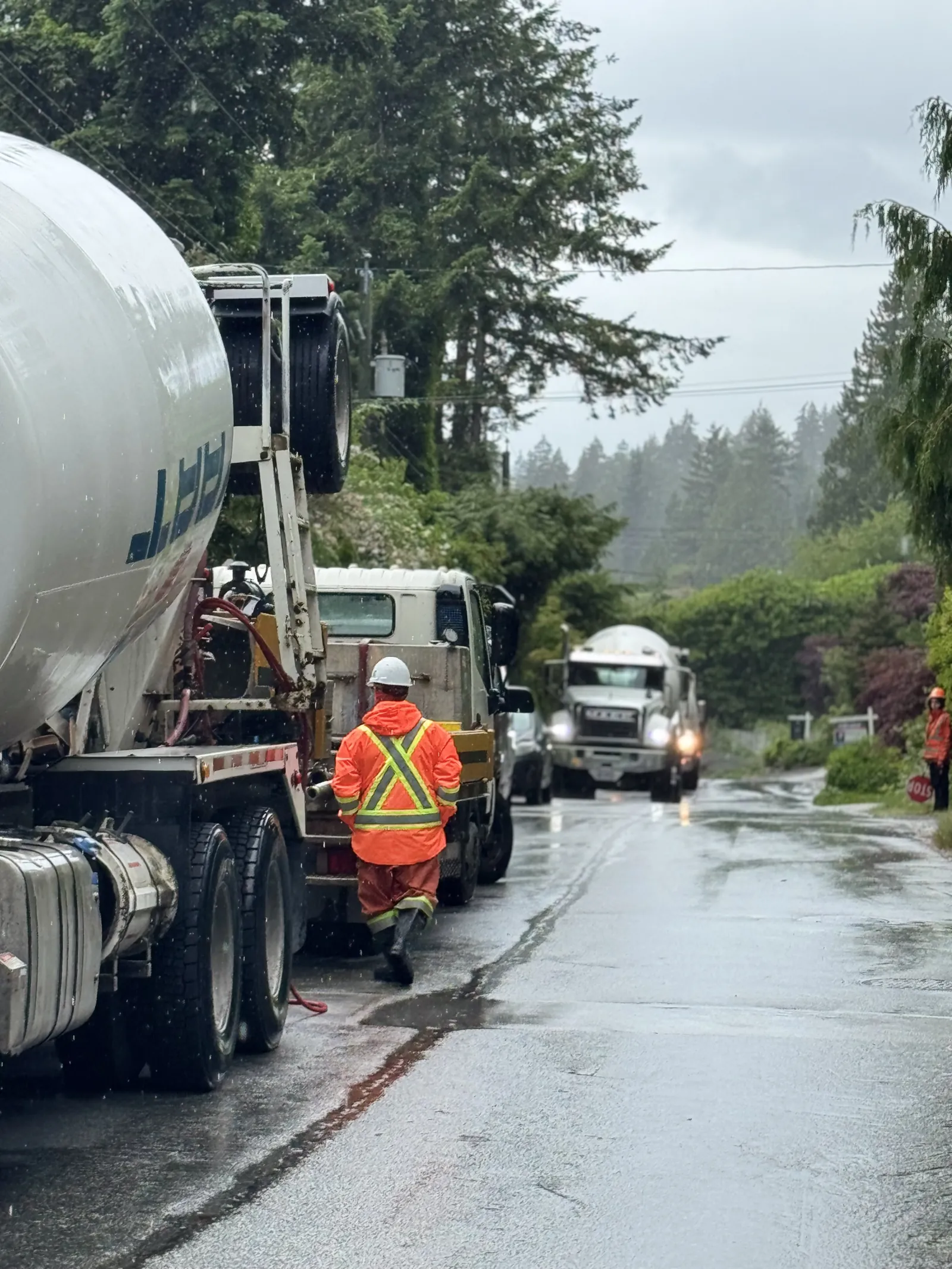 Concrete mixer trucks on a wet, tree-lined North Shore street during a rainy Eurohouse pour