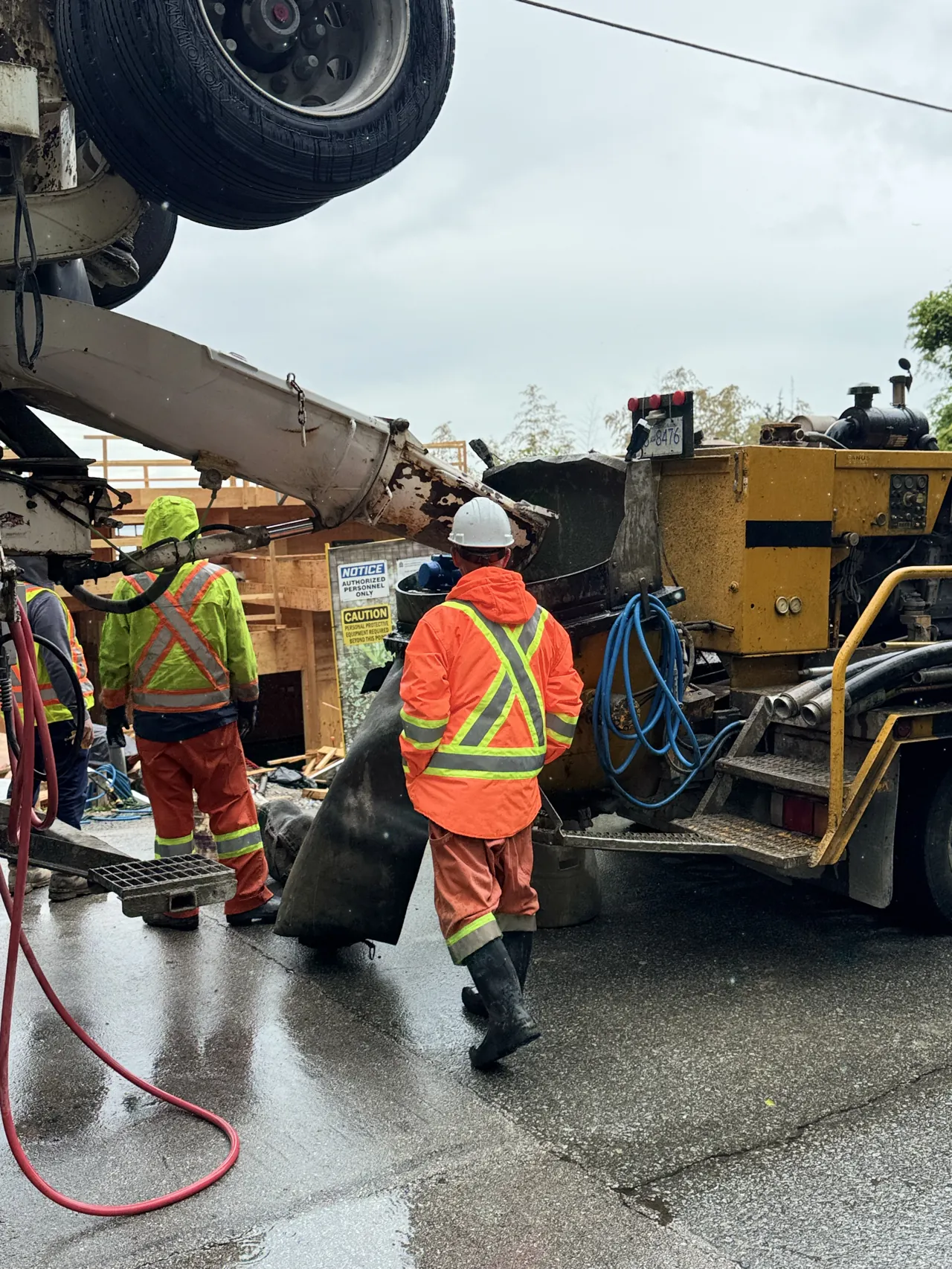 Eurohouse crew in rain gear operating a concrete pump truck on a wet West Vancouver street feeding a covered pour