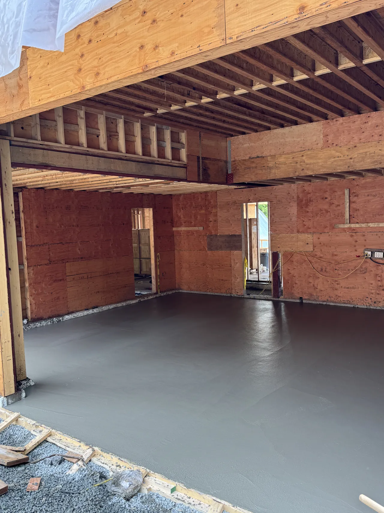 Finished interior concrete slab curing under the roof of a framed North Shore home, protected from rain and ready for floor finishes