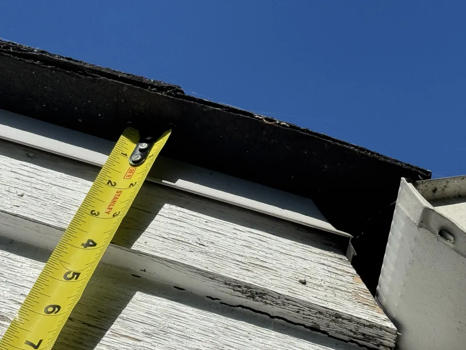 Measuring tape on deteriorated fascia trim during repair scoping on a strata building