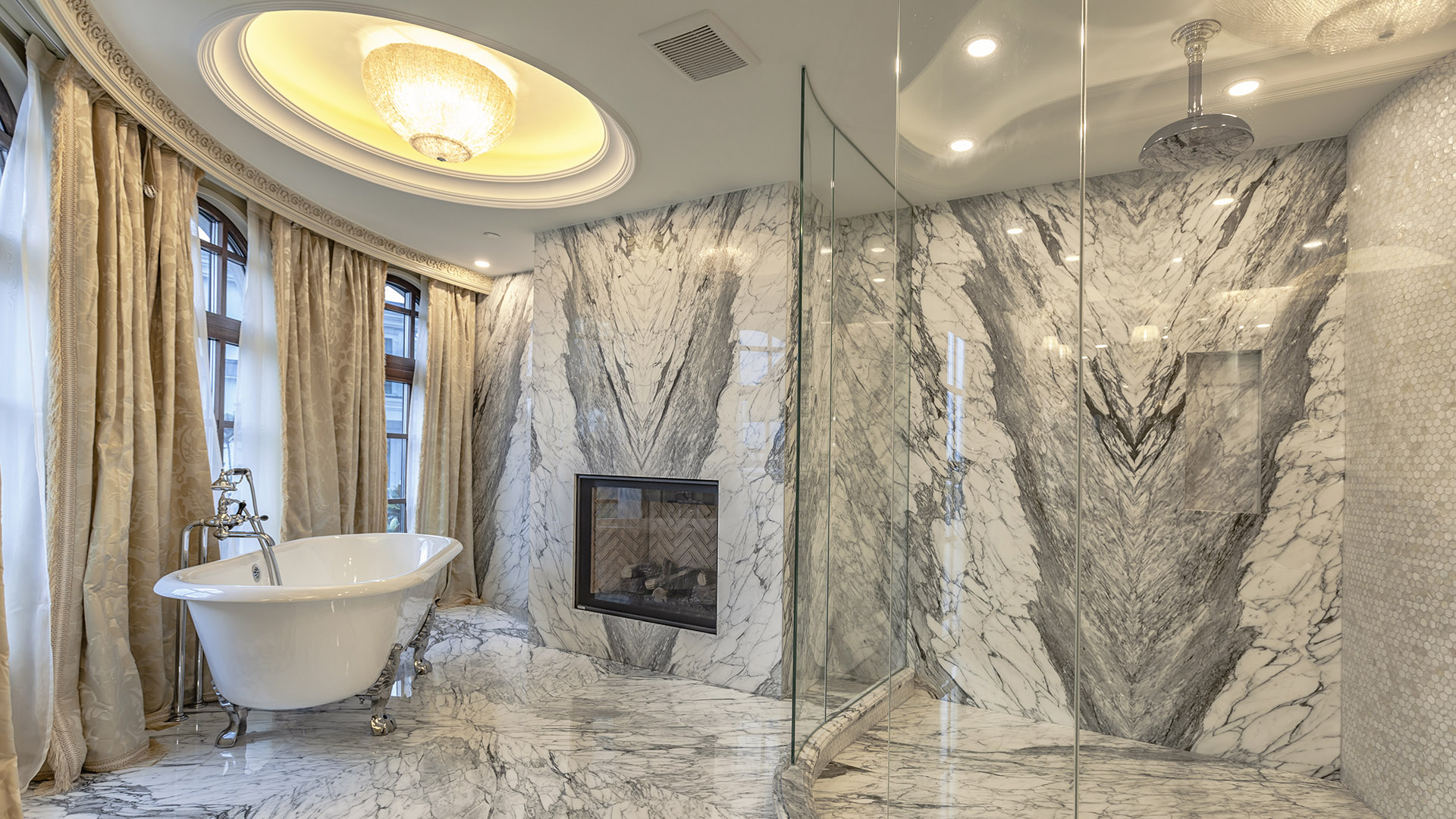 Ambleside Palace master bathroom with book-matched marble walls freestanding soaker tub and fireplace in West Vancouver