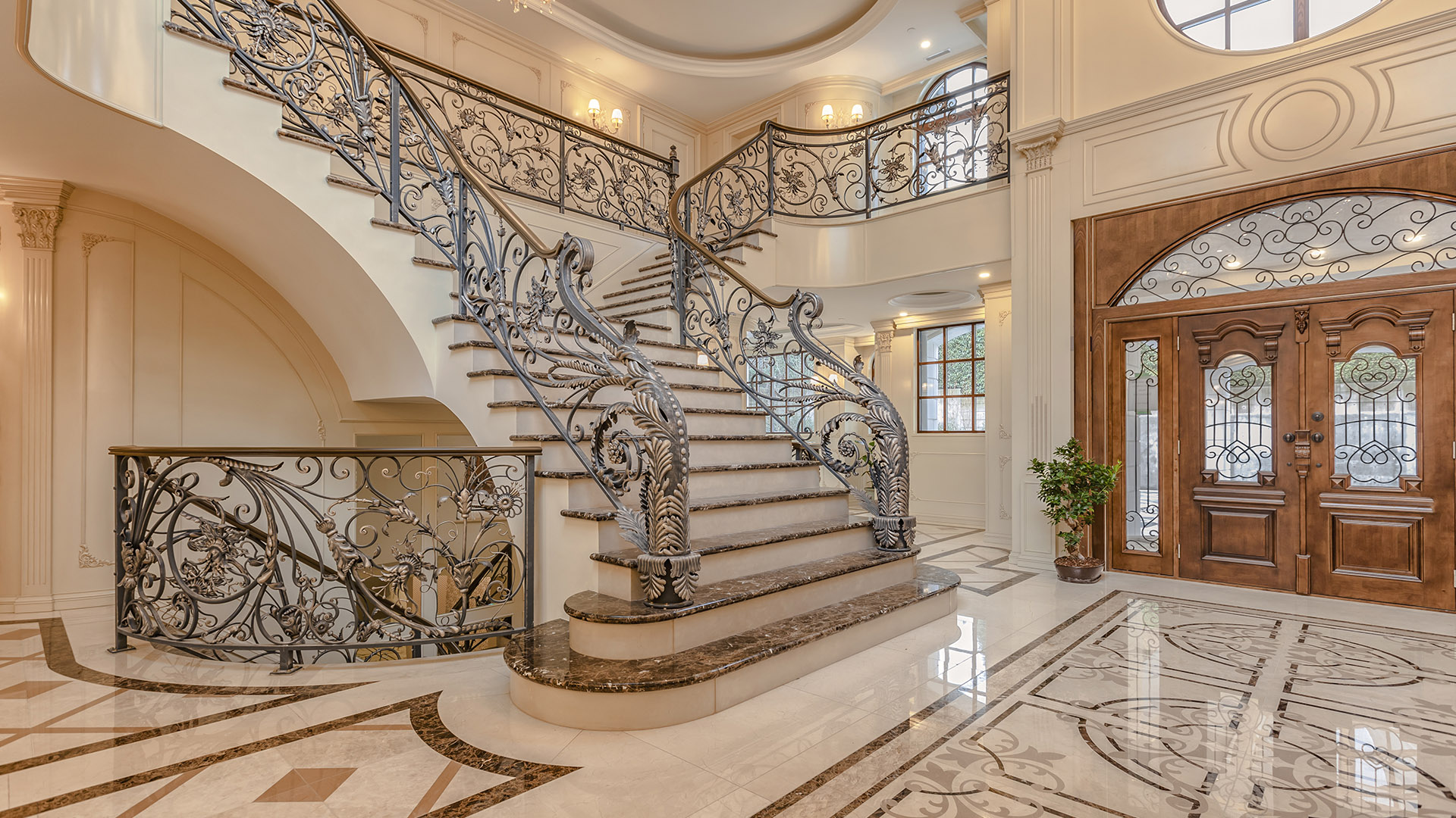 Ambleside Palace foyer entry with curved staircase ornate iron railing and leaded glass front door in West Vancouver