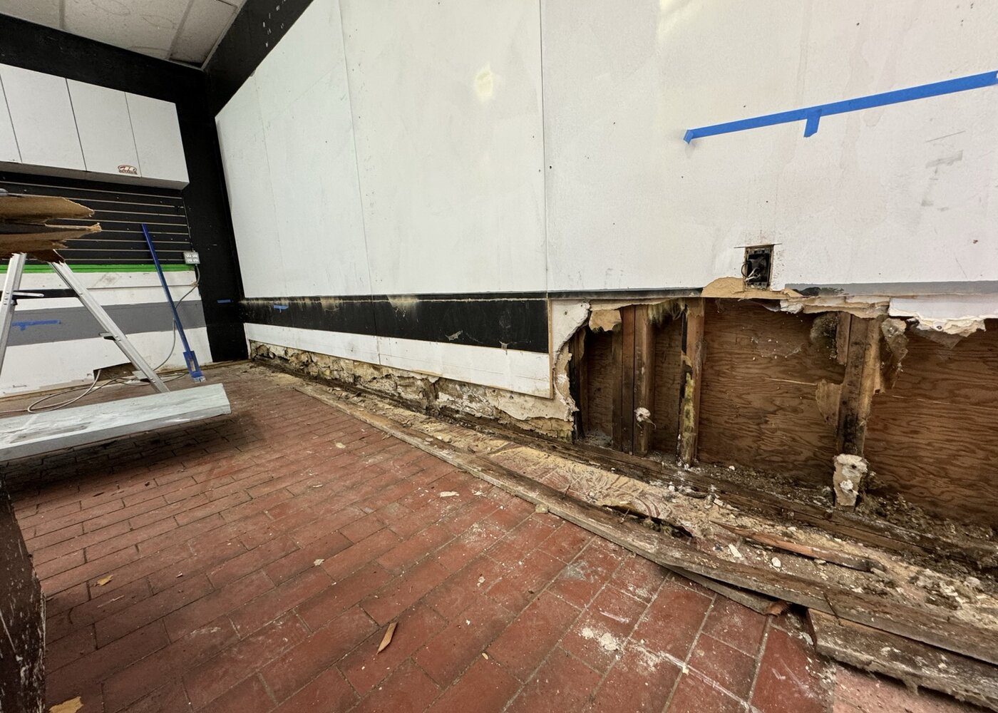 Exposed water-damaged baseboards and drywall in West Broadway retail space showing rotted framing and compromised wall cavity