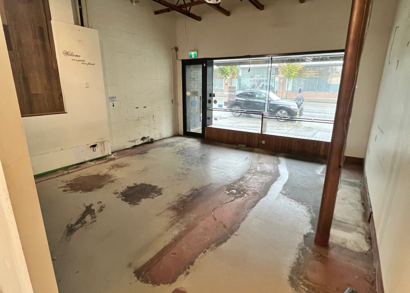 Stripped retail interior during demolition phase showing exposed concrete floor, removed fixtures, and storefront window on West Broadway