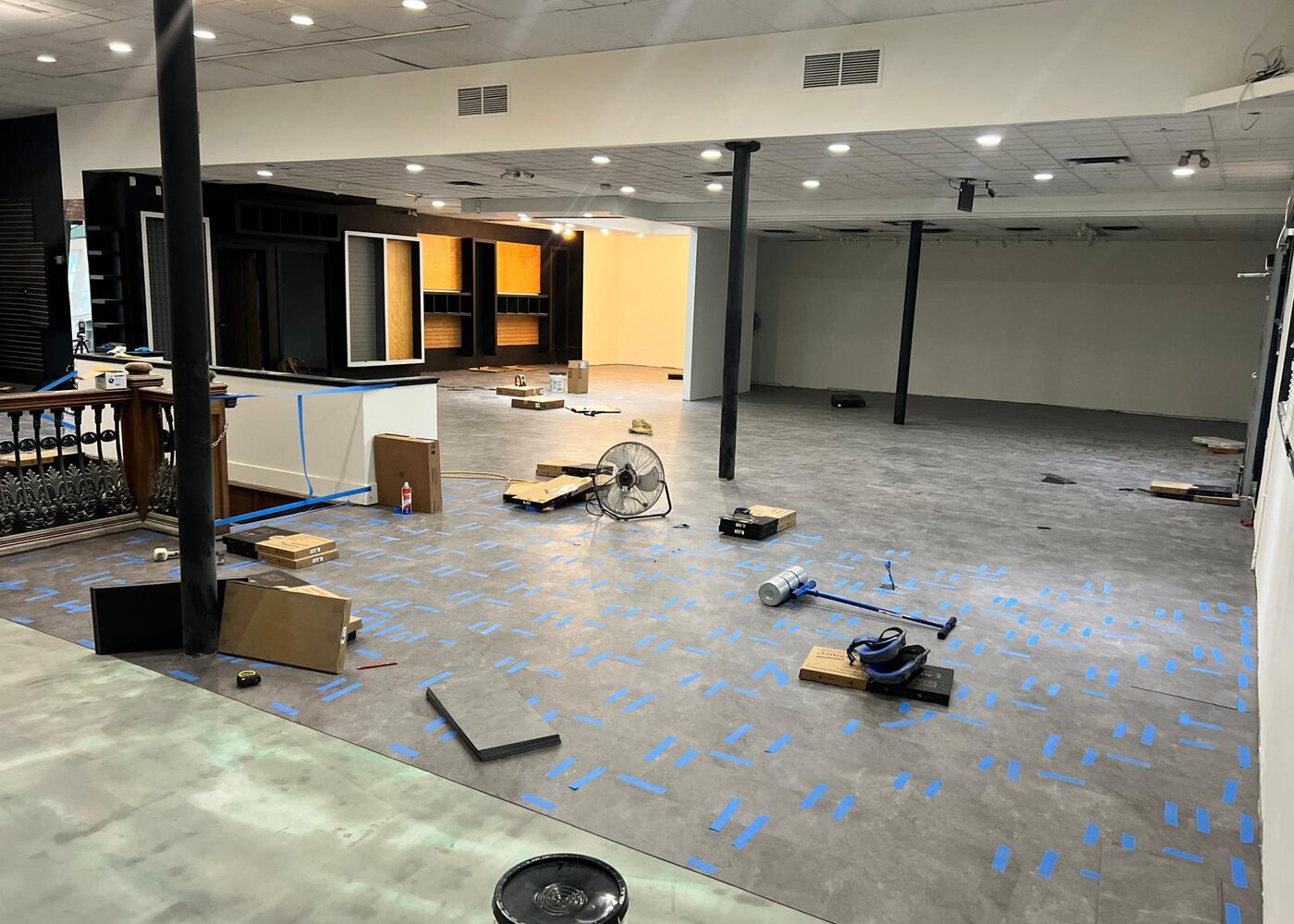 New flooring being installed with blue tape spacing while custom front desk and cabinetry take shape in retail restoration