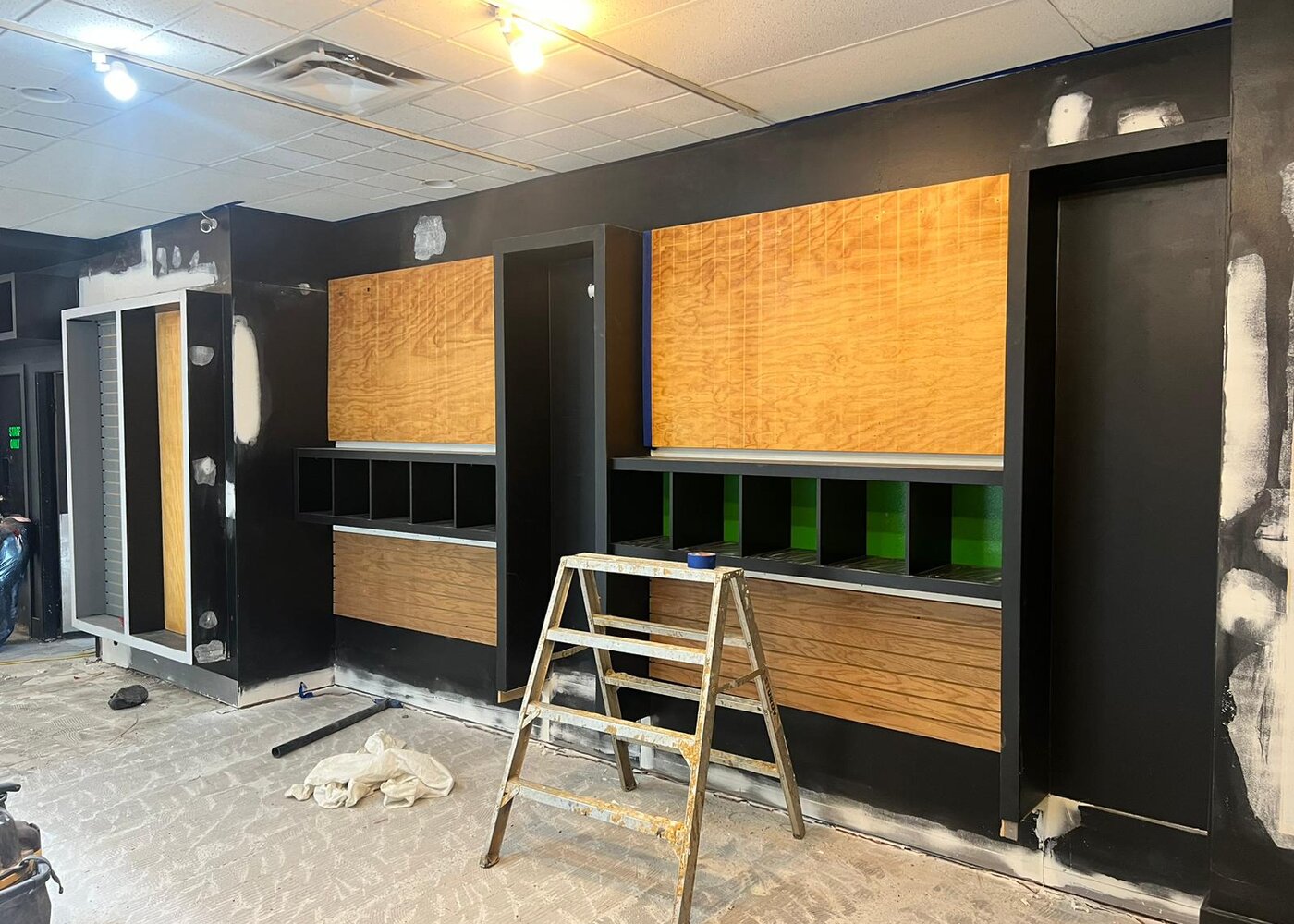 Custom oak-veneered millwork and cabinetry being installed in restored retail space with black finish and natural wood panels