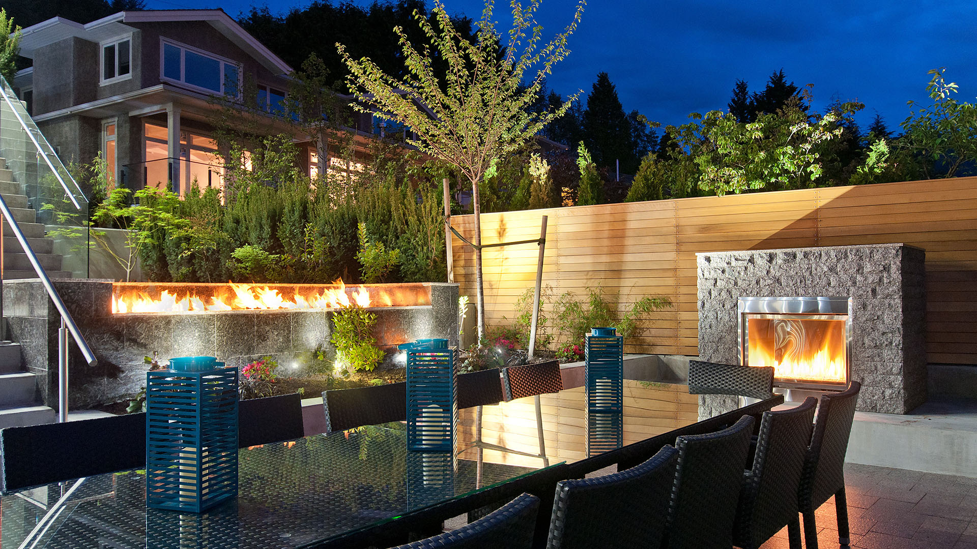Outdoor dining terrace with linear fire wall freestanding granite outdoor fireplace cedar fence and tiered landscaping Millstream British Properties West Vancouver