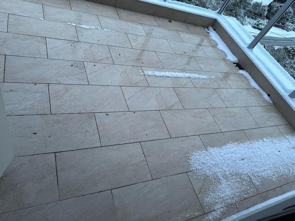 Completed balcony deck with new tiles and electrically heated snow melting system at Newdale Court North Vancouver — deck surface remains clear while snow accumulates at edges proving system effectiveness