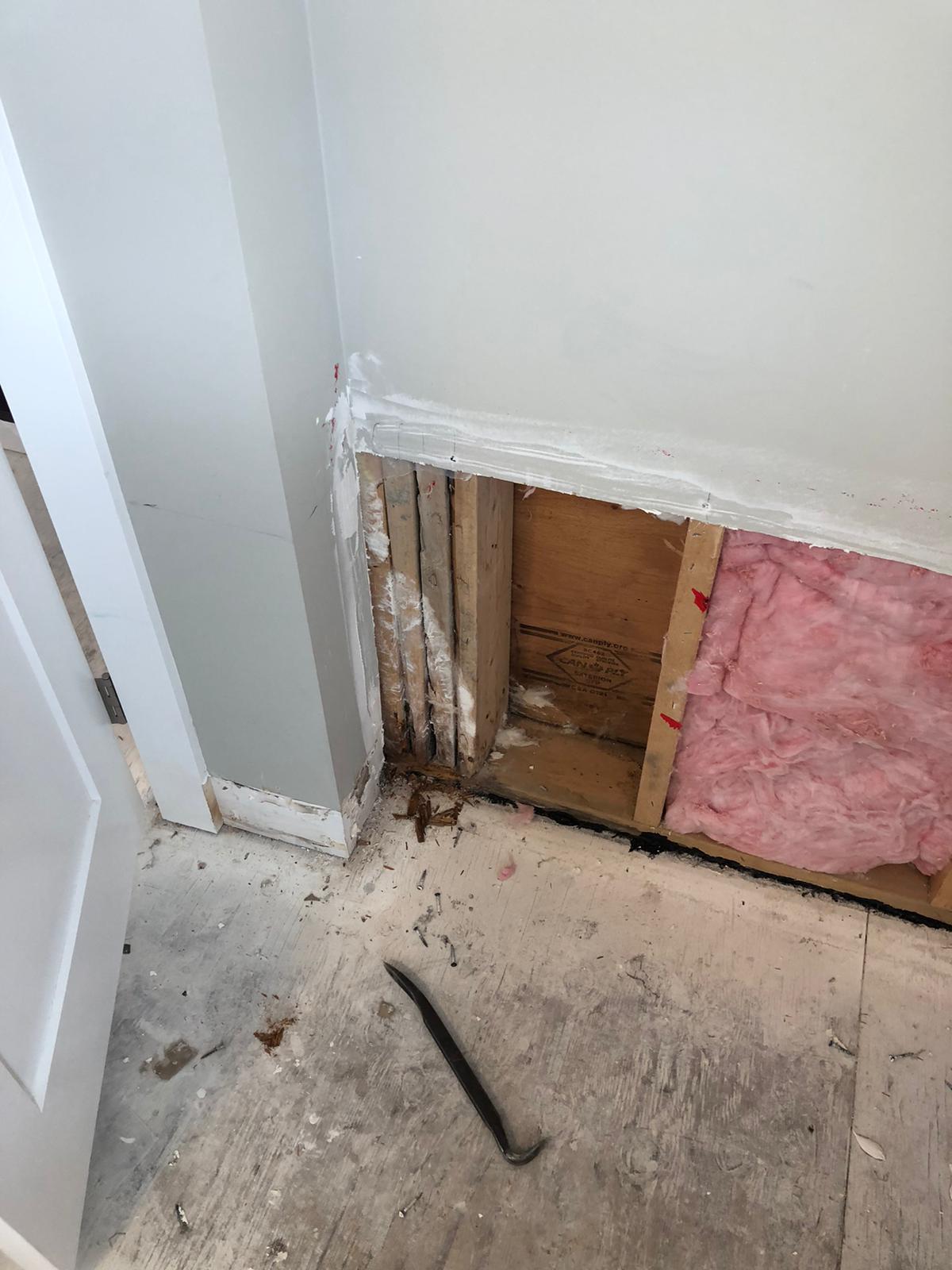 Exterior wall opened during insurance restoration at Newdale Court revealing water-damaged framing and pink fiberglass insulation behind drywall