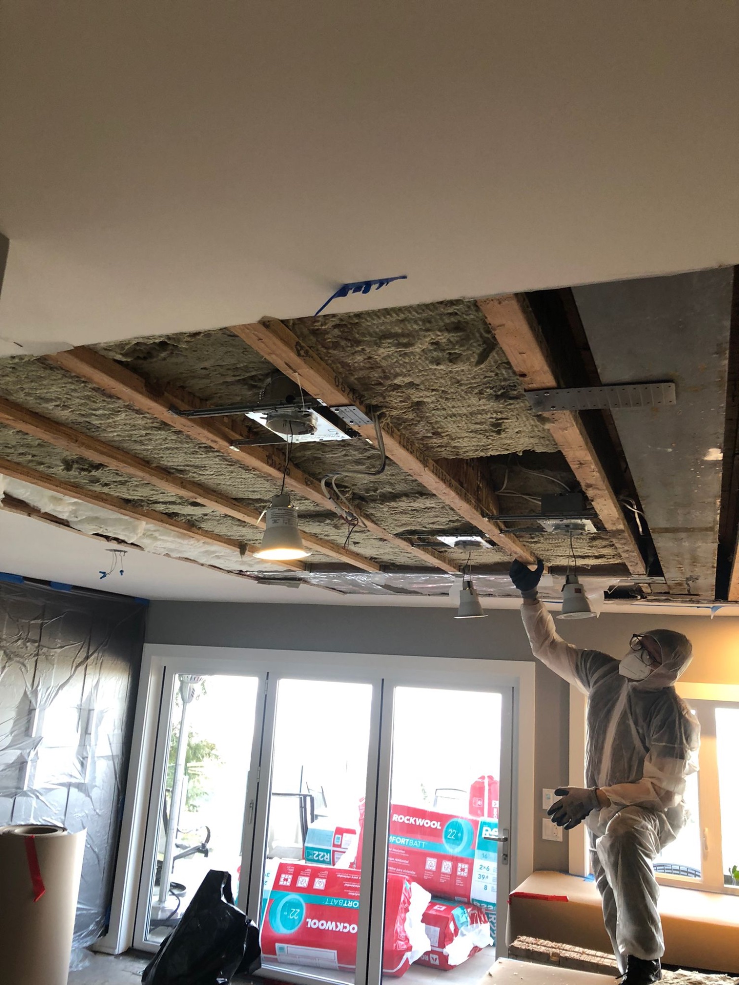 Water-damaged ceiling drywall removed exposing floor joists and old insulation at Newdale Court with Rockwool insulation staged for reinstallation