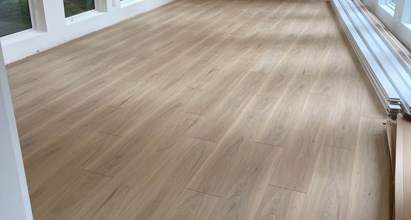 Completed insurance restoration showing new laminate flooring in luxury North Vancouver living room with skylights, pot lights, fireplace feature wall, and floor-to-ceiling windows overlooking trees