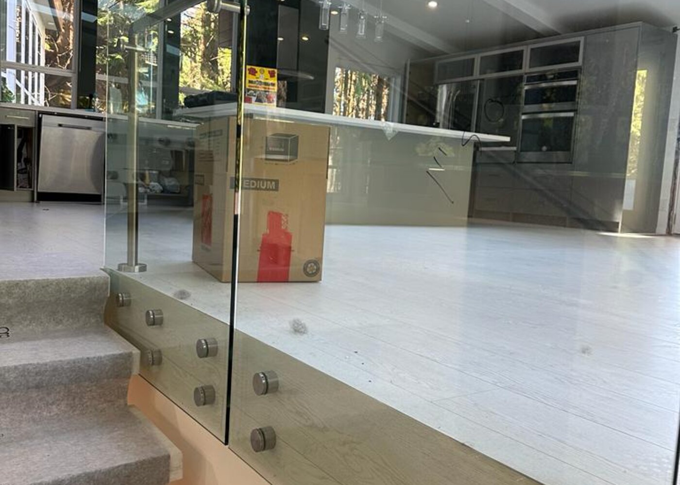 Kitchen viewed through glass railing with original flooring and stainless steel appliances visible in North Vancouver luxury home