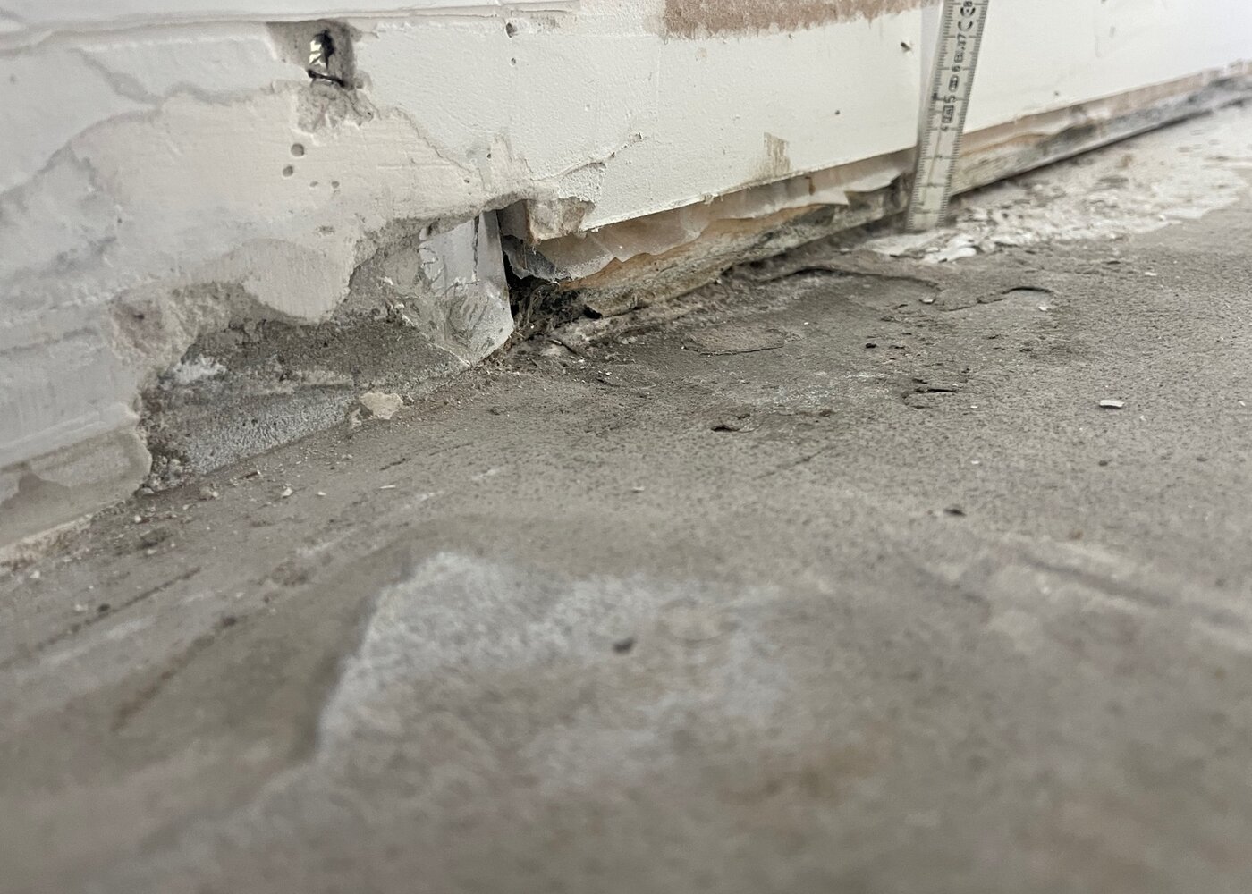 Damaged subfloor along wall with crumbling concrete, holes, and water staining from long-term moisture exposure