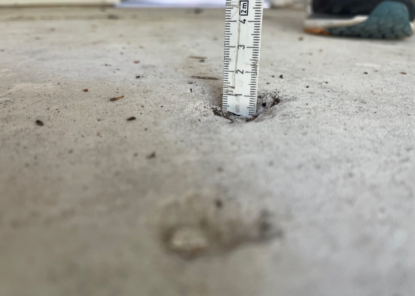 Tape measure inserted into subfloor hole showing depth of deterioration and evidence of significant void beneath surface
