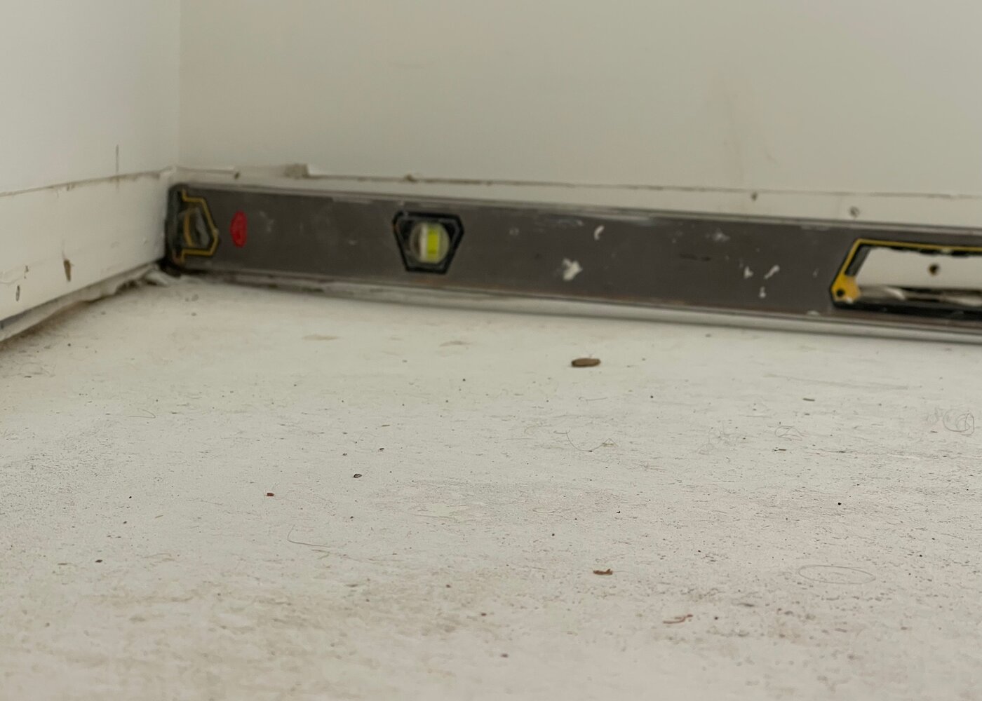 Spirit level on uneven subfloor showing significant deviation from flat after flooring removal — evidence supporting self-levelling compound change order