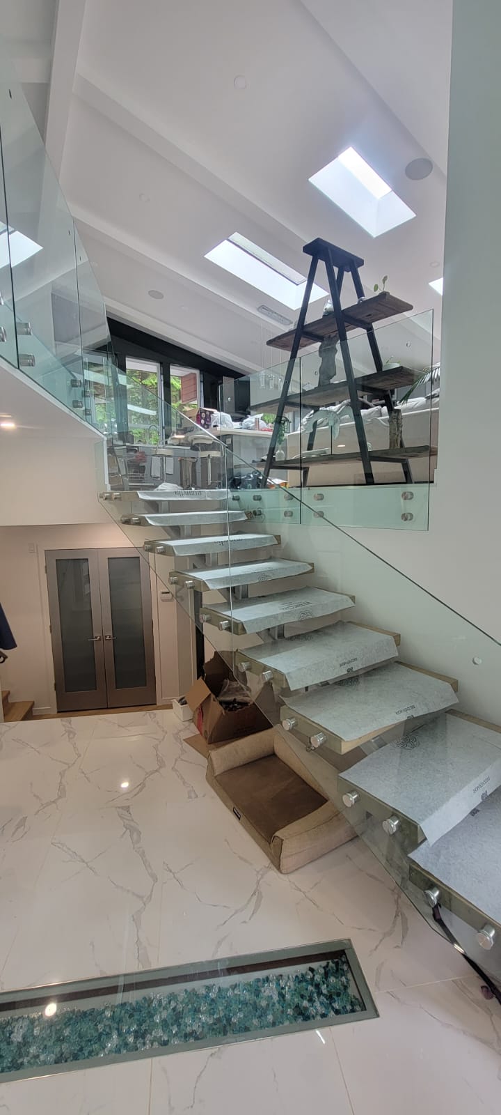 Floating staircase with glass railing, marble treads, skylights, and decorative glass floor feature during restoration at Prospect Road North Vancouver by Eurohouse Construction