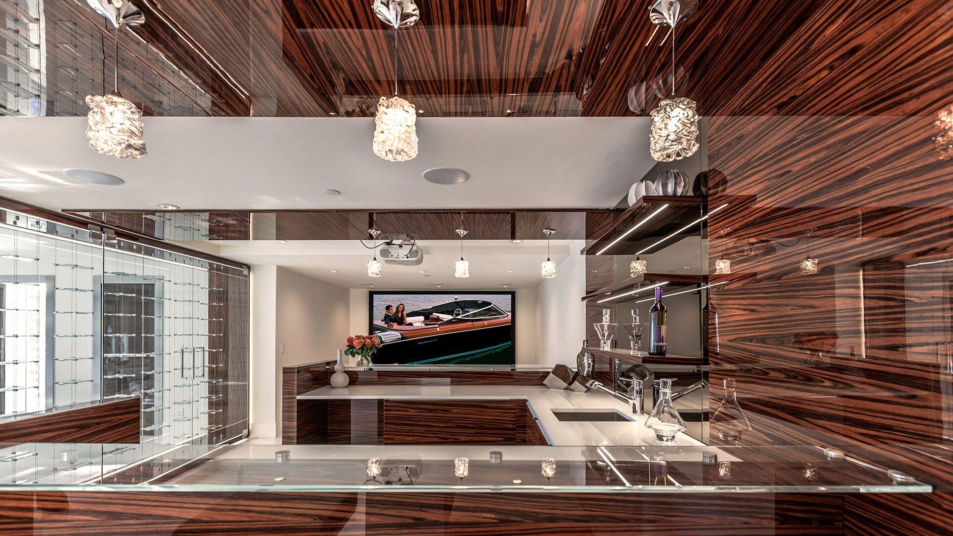Entertainment bar detail with zebrawood ceiling panels Riva speedboat projected on screen glass wine cellar and crystal pendant lighting at The Riva Club designed and installed by Eurohouse Construction