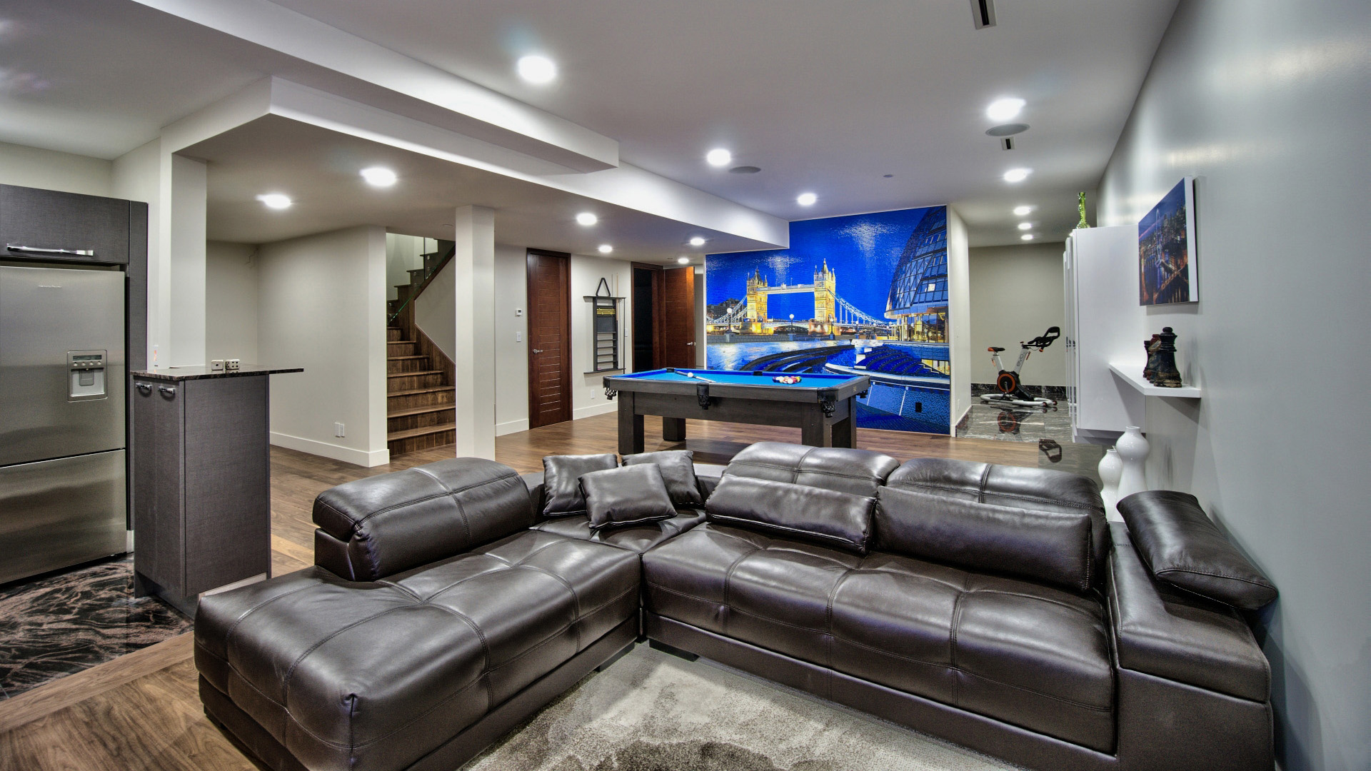 Lower level games room with pool table custom Tower Bridge mosaic tile mural leather sectional and gym equipment West Bay West Vancouver