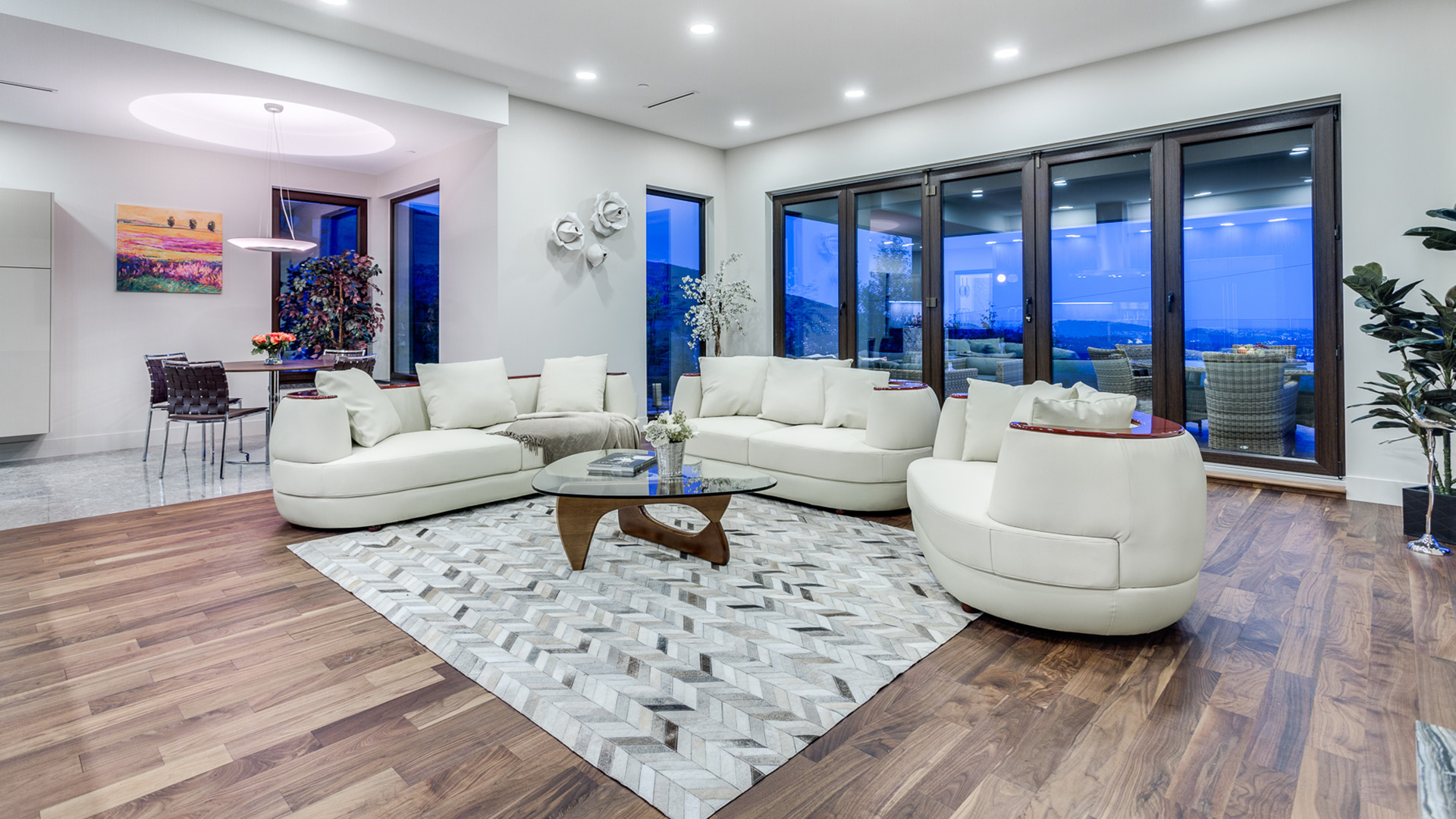Family room at dusk with walnut flooring white sectional folding doors leading to outdoor terrace West Coast Contemporary British Properties West Vancouver