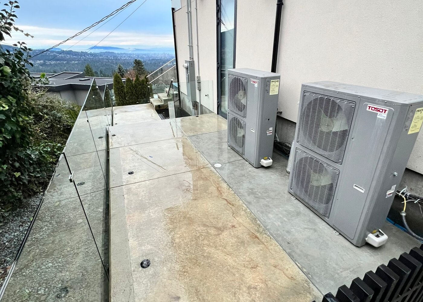 Completed exterior with restored concrete deck, TOSOT HVAC units, and glass railings overlooking West Vancouver views