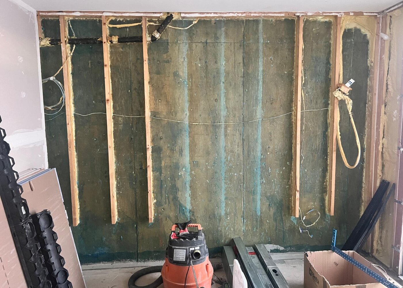 Interior basement wall with drywall removed showing exposed concrete foundation with water staining and new framing installed