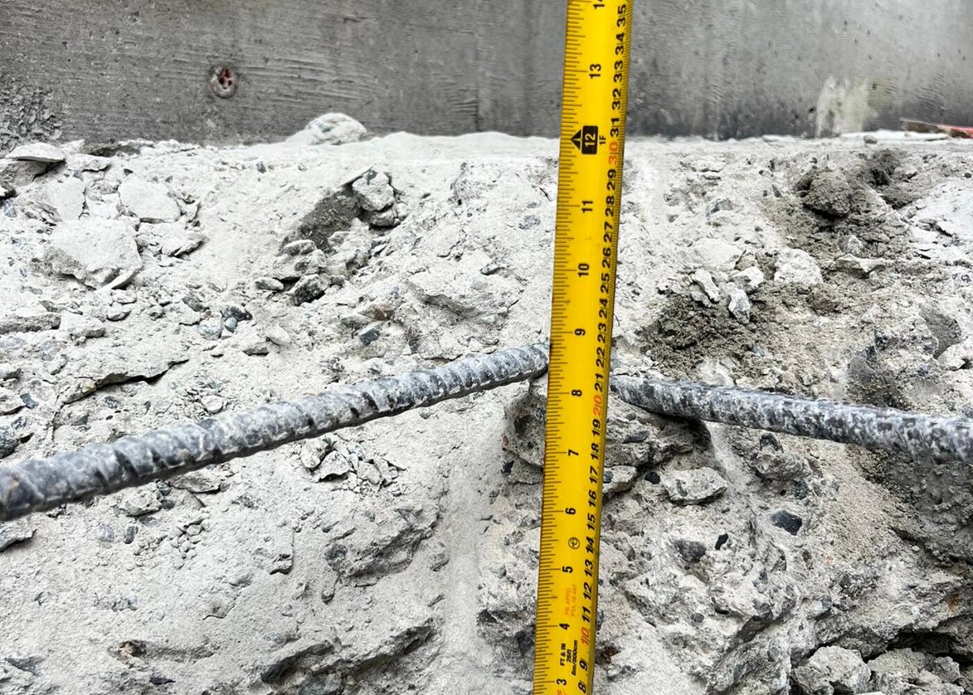 Tape measure showing depth of excavation and exposed rebar at concrete foundation during structural assessment